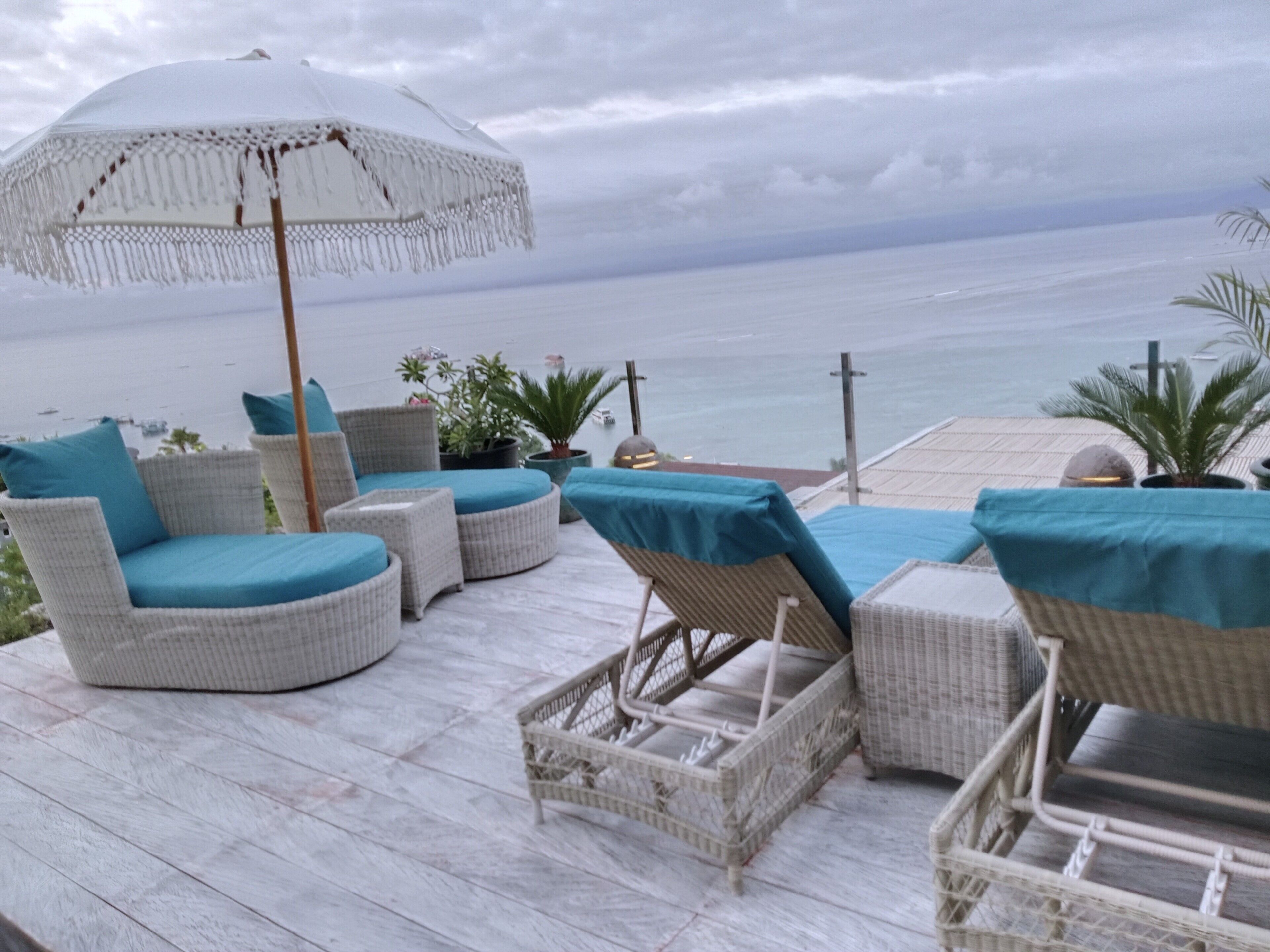 Una terraza con mobiliario de mimbre y una sombrilla blanca, con vistas a una masa de agua.
