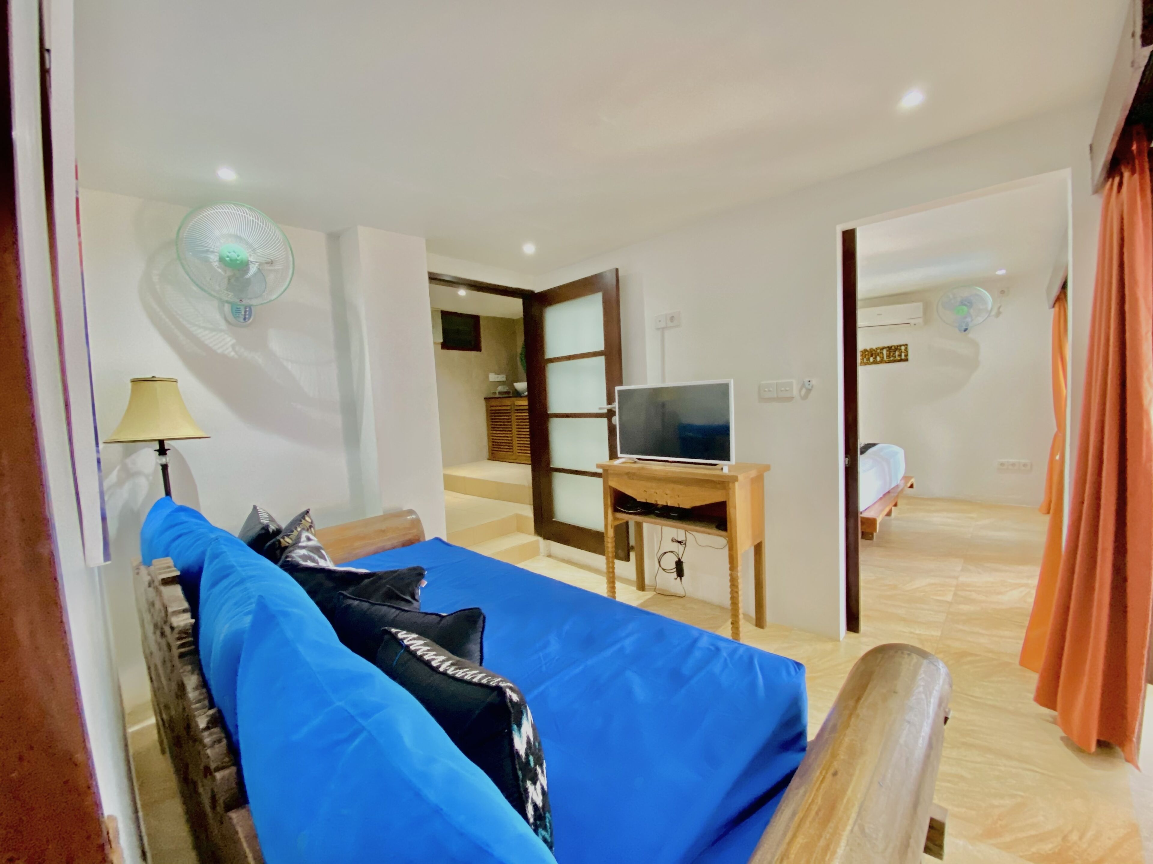 A room with a bed, a TV on a wooden stand, a desk, and a mirror.