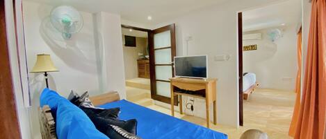 A room with a bed, a TV on a wooden stand, a desk, and a mirror.