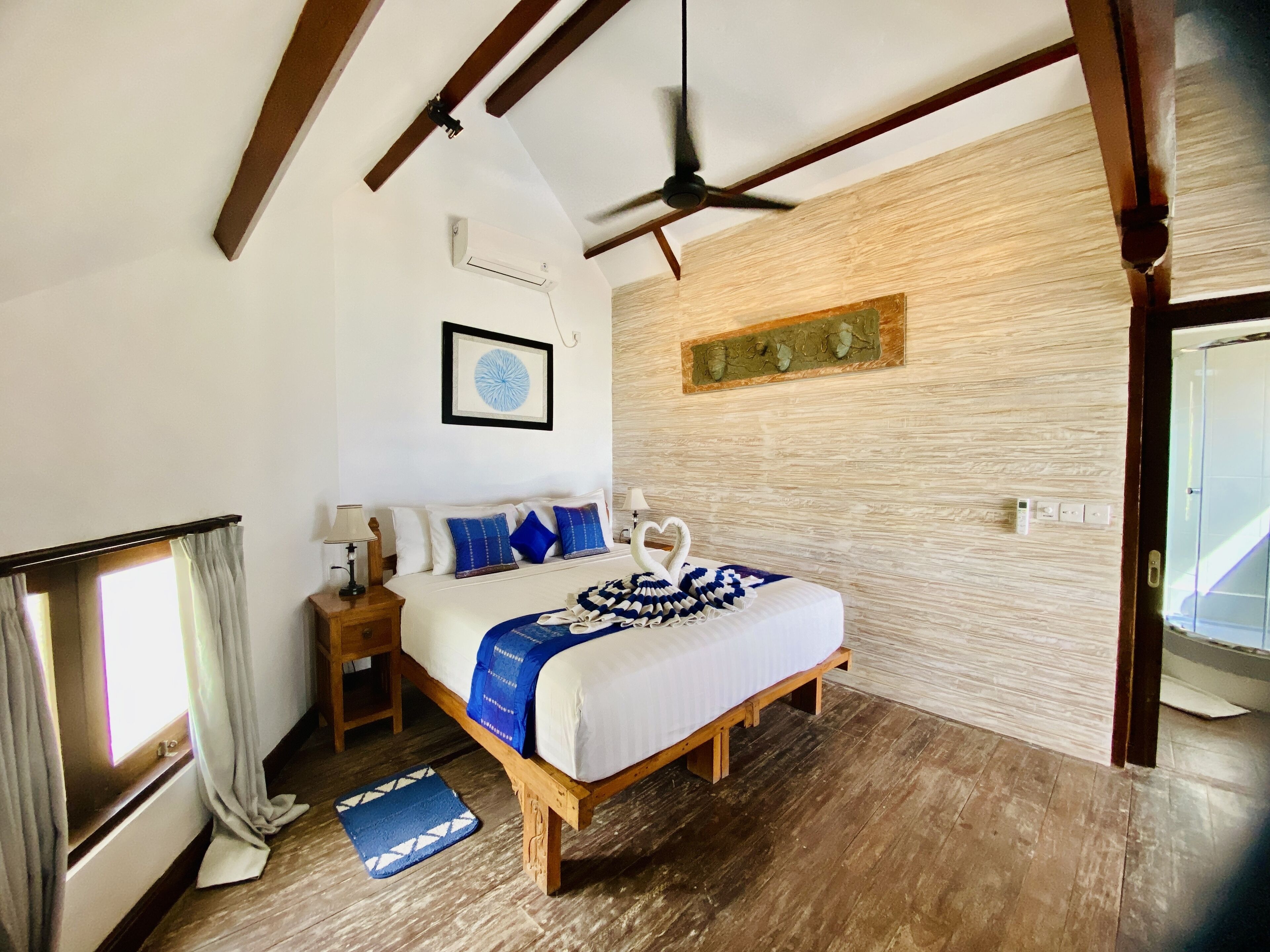 A bedroom with a wooden bed, a ceiling fan, a wall-mounted air conditioner, and a window with curtains.