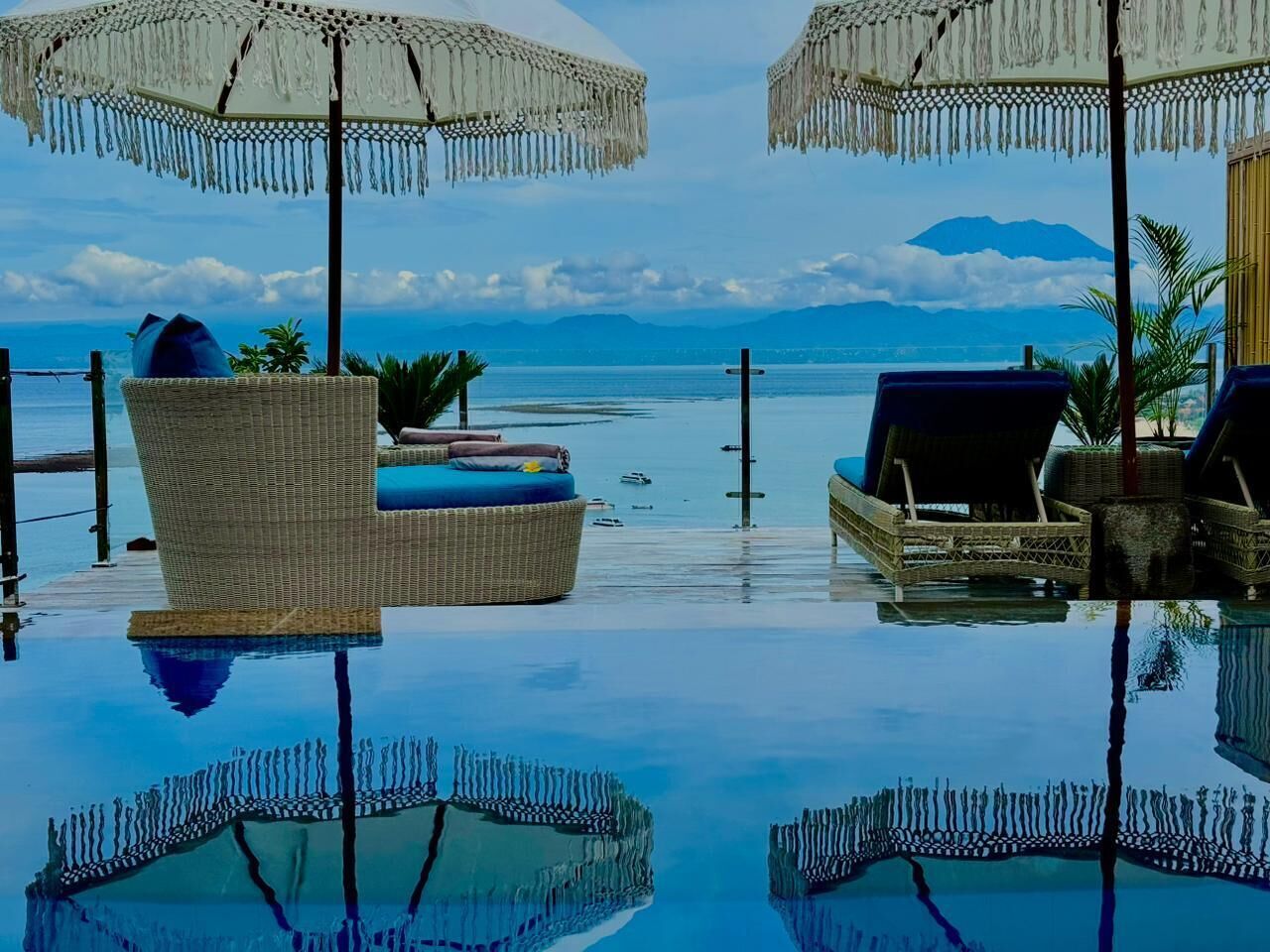 Une piscine à débordement dotée de chaises longues et de parasols, offrant une vue dégagée sur la mer et les montagnes.