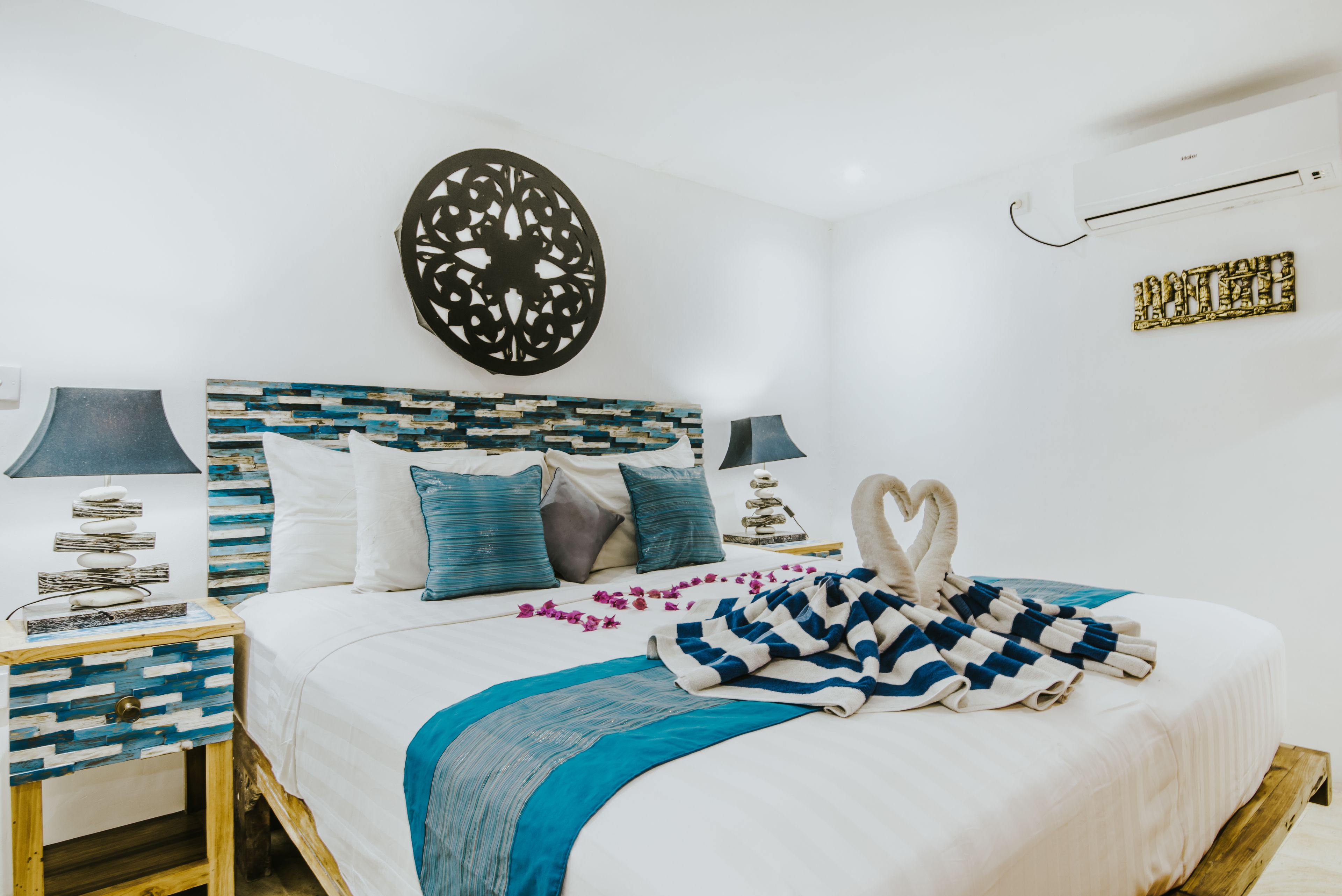 A neatly arranged bedroom with a bed, pillows, a decorative wall piece, and a bedside table with a lamp.