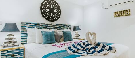 A neatly arranged bedroom with a bed, pillows, a decorative wall piece, and a bedside table with a lamp.