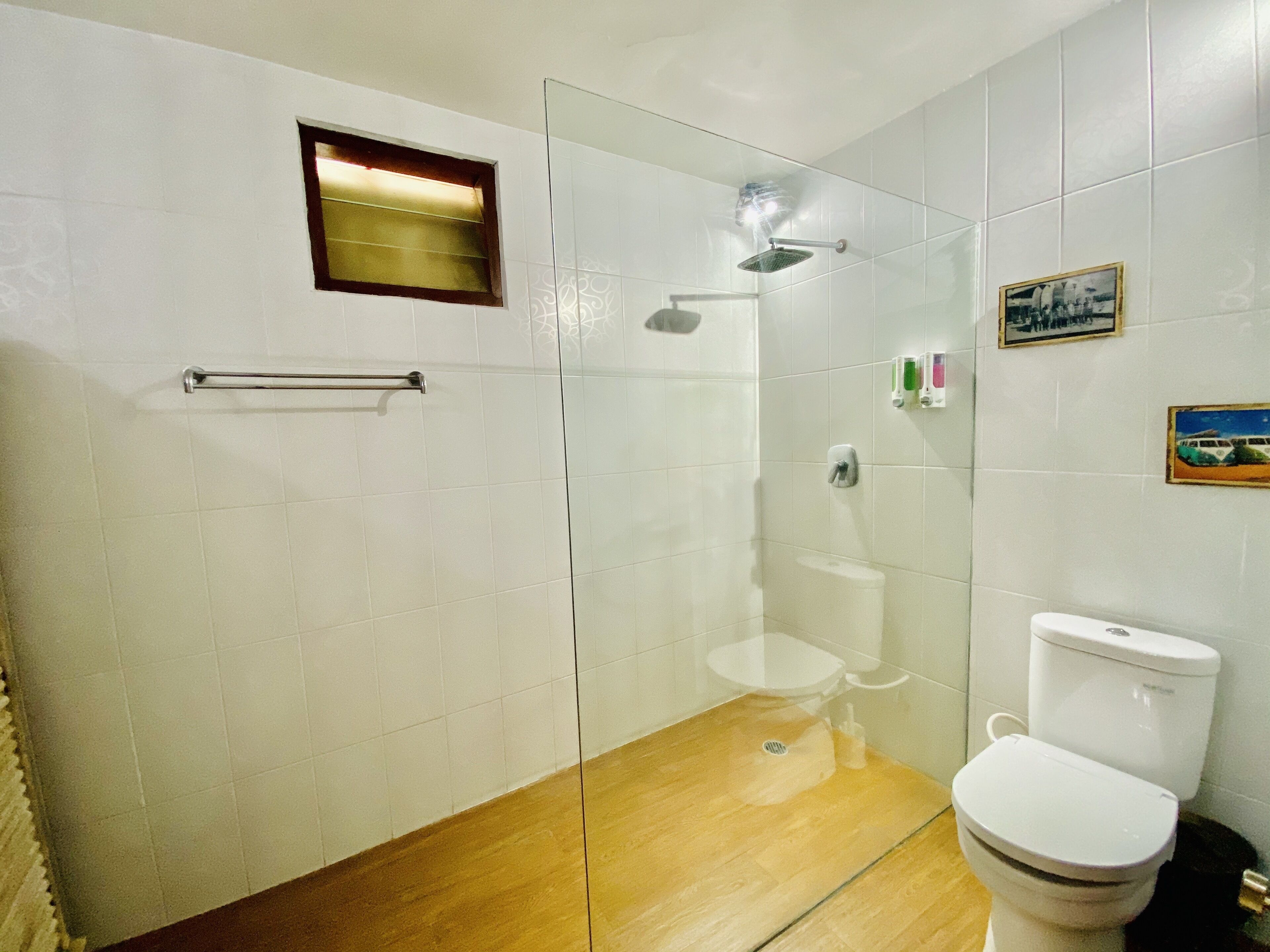 A bathroom with a glass-enclosed shower, a toilet, and a small window.