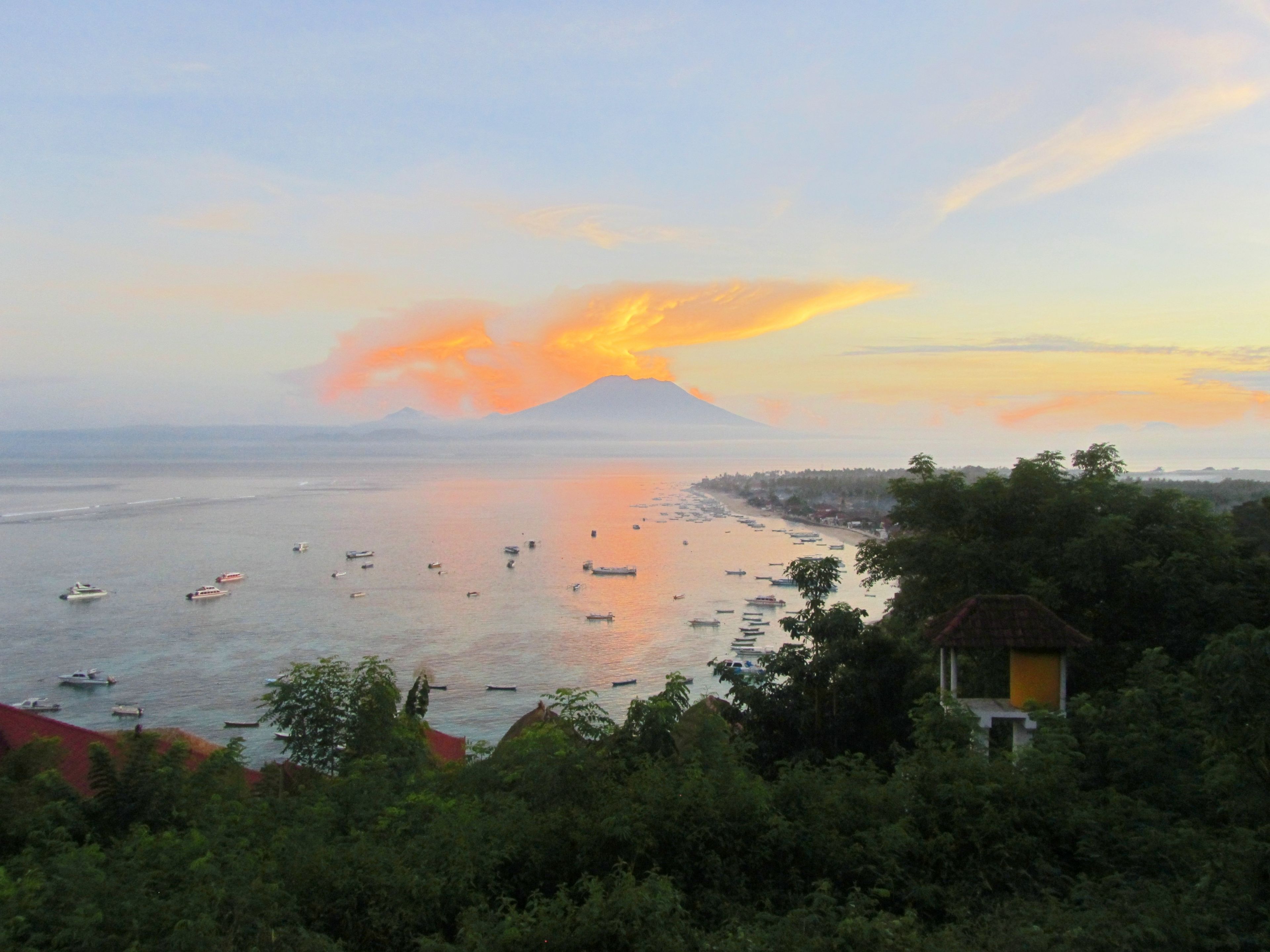 A coastal view with boats on the water, a mountain in the background, and a building on the right.