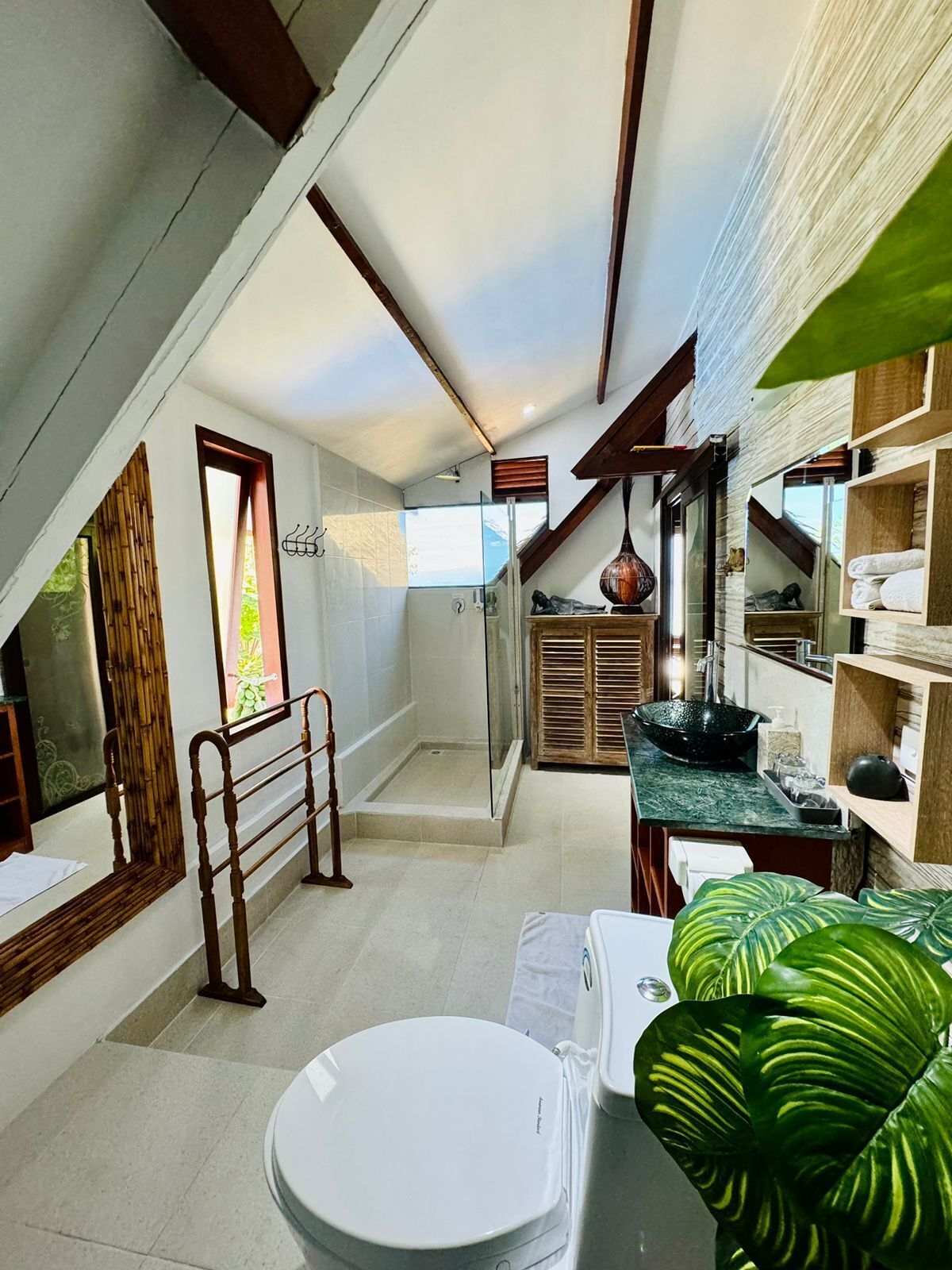A modern bathroom with a freestanding bathtub, a shower, and a toilet. There is a window providing natural light and a view of the outdoors.