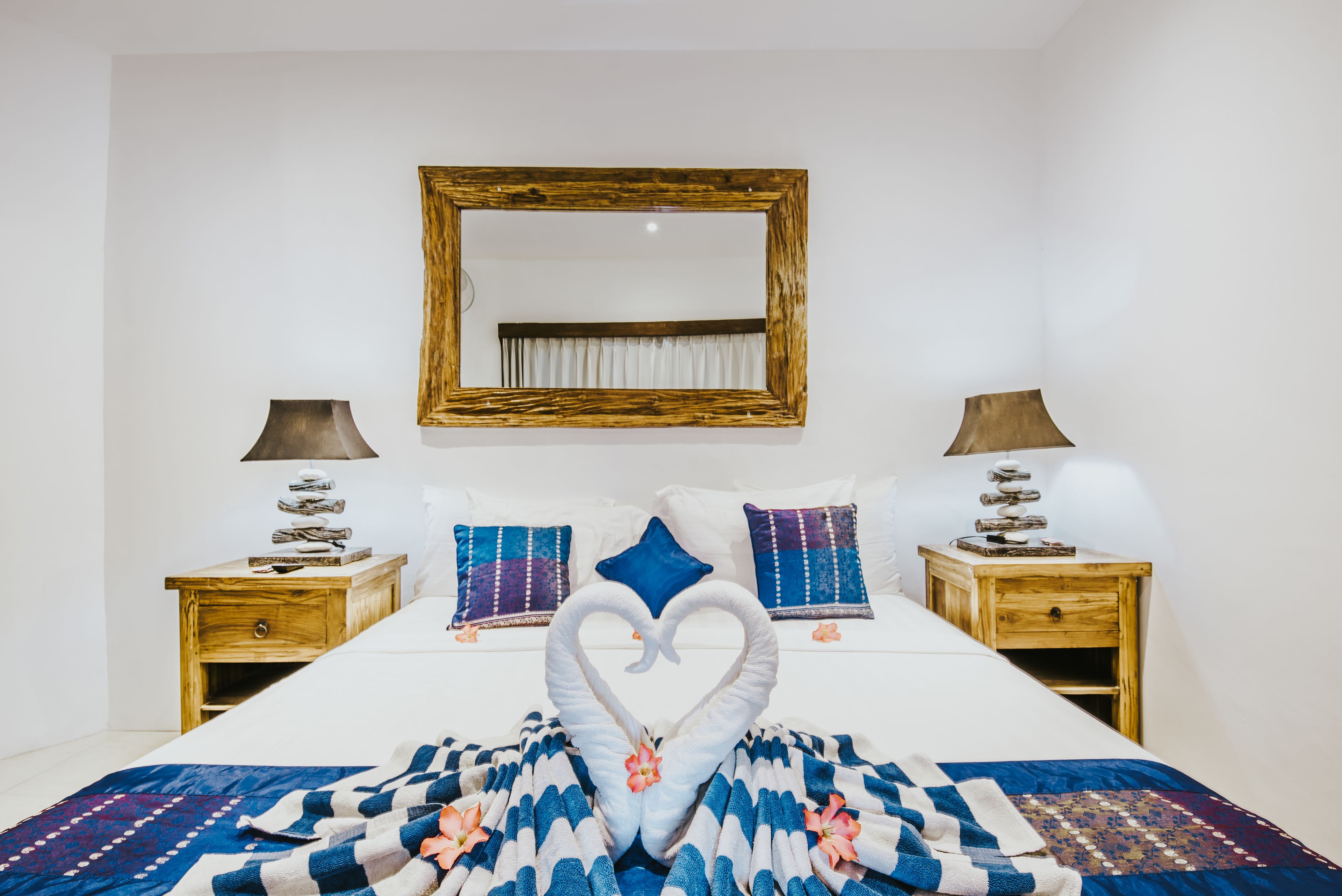 Una habitación de hotel con una cama, dos mesitas de noche, un espejo y almohadones decorativos.