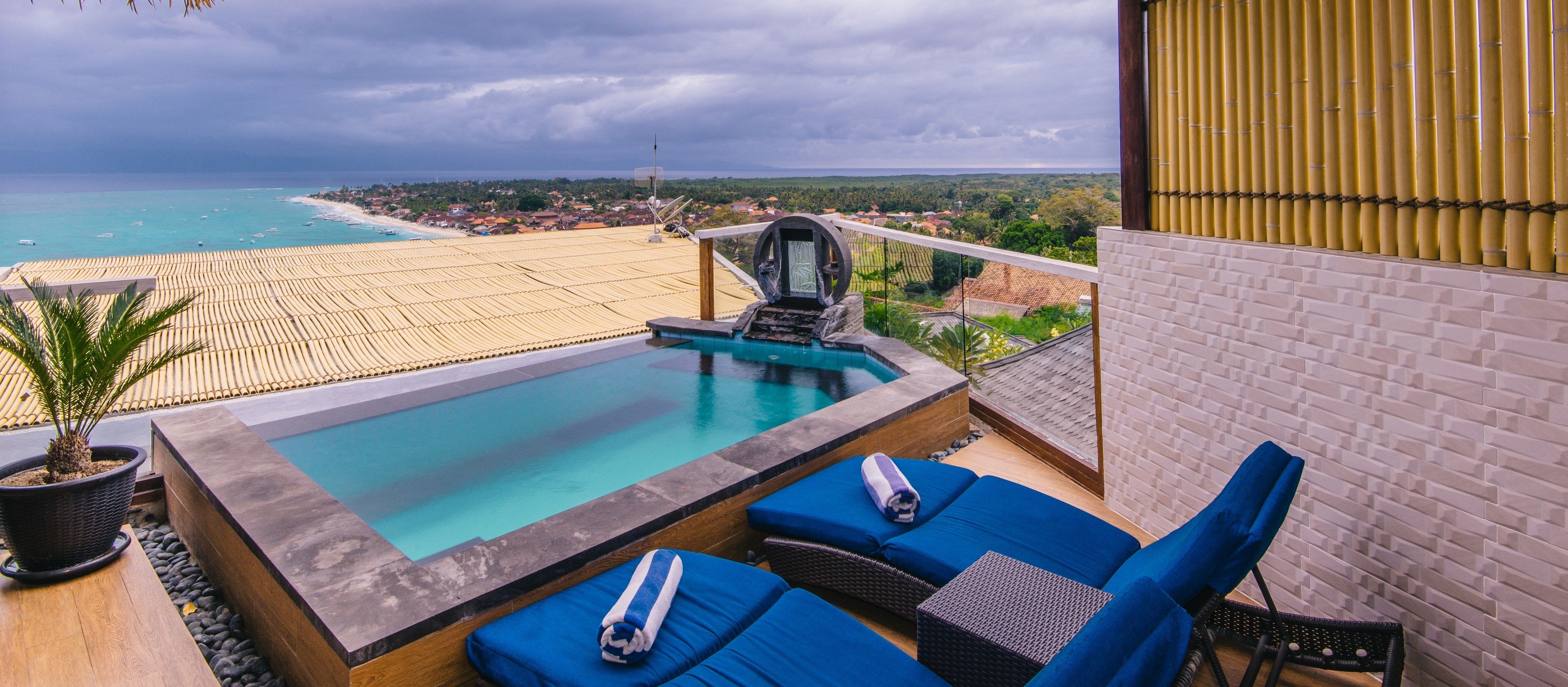 A rooftop pool with blue lounge chairs and a potted plant.