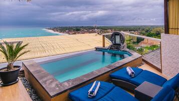 A rooftop pool with blue lounge chairs and a potted plant.