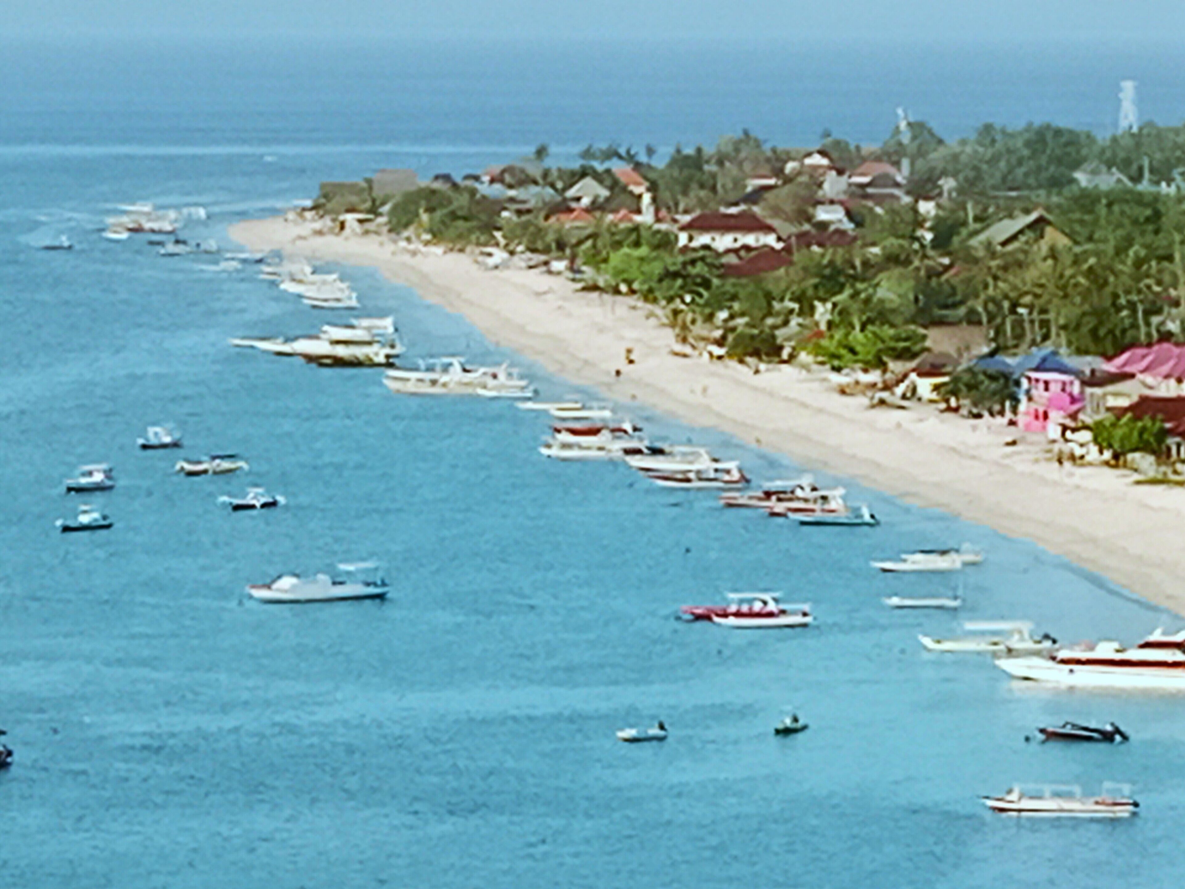 A coastal area with a beach lined with houses and boats anchored in the water.