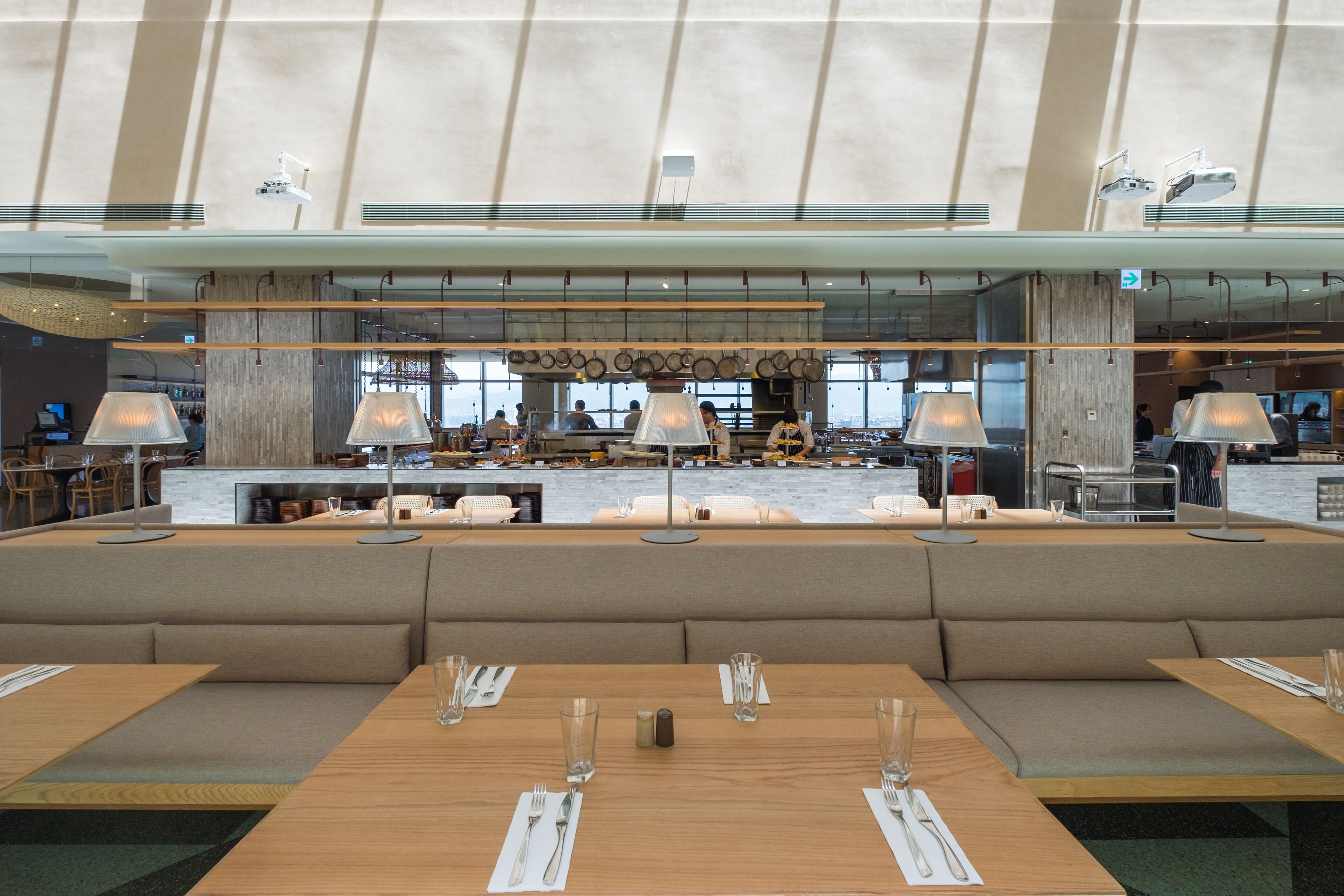 A modern restaurant with a long counter, cushioned seating, and pendant lighting.