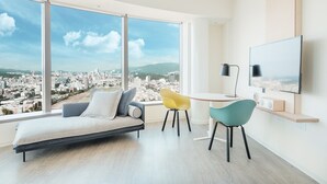 A modern bedroom with a large window, a bed, a desk with two chairs, a TV, and a city view. - amba Taipei SongShan (Taipei)