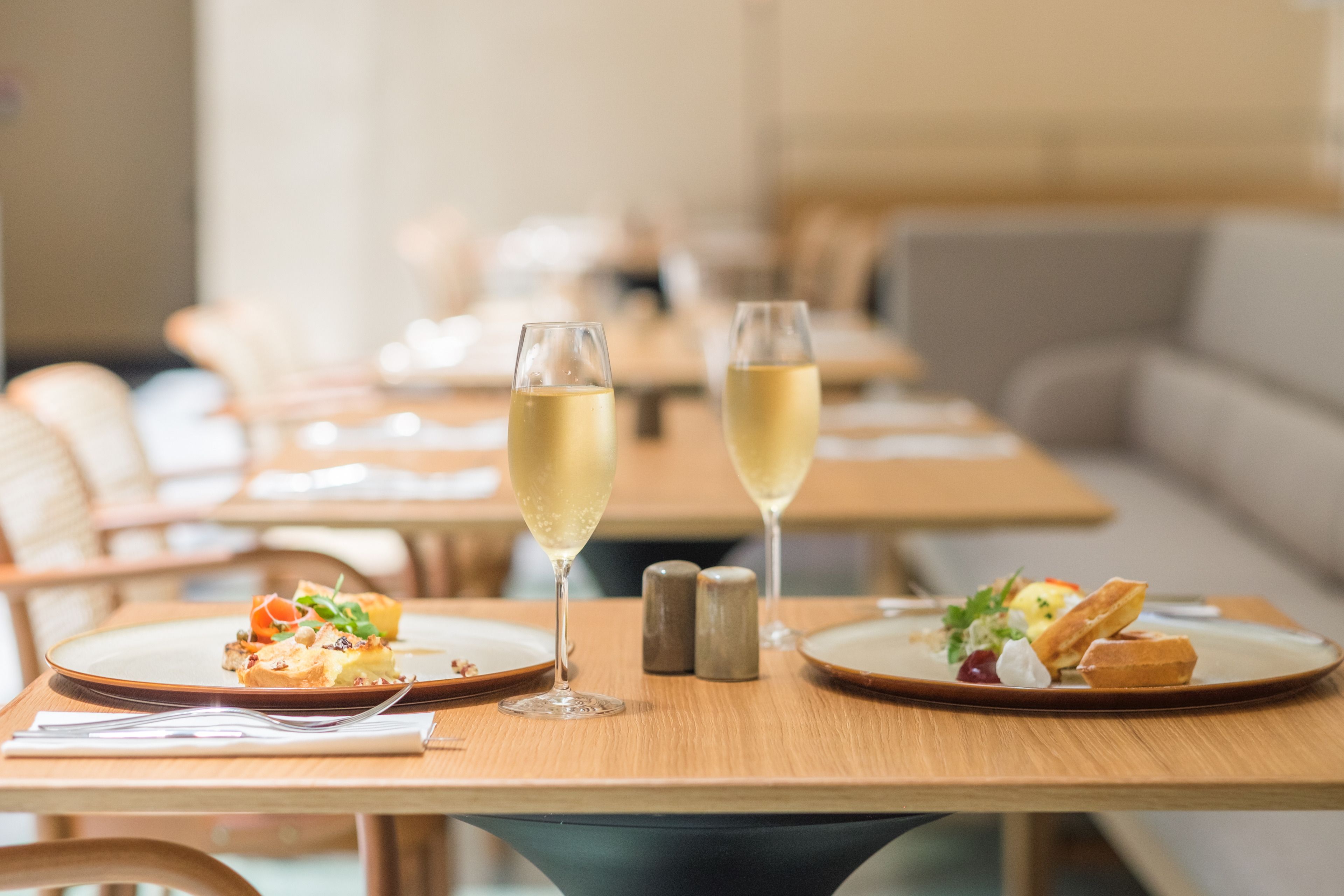 A dining table with two glasses of white wine, salt and pepper shakers, and plates of food.