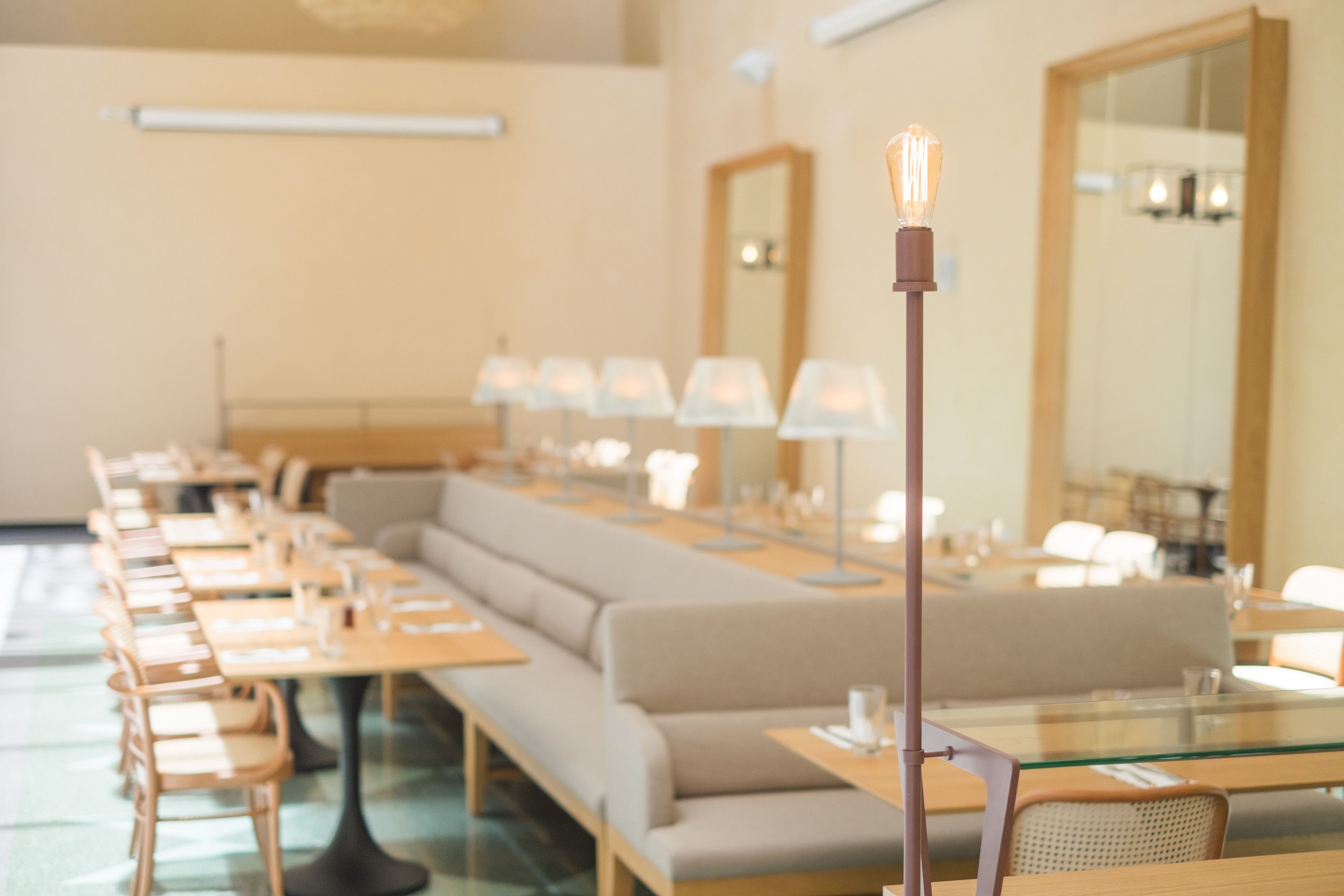 Un comedor moderno con mesas largas, asientos acolchados e iluminación colgante.