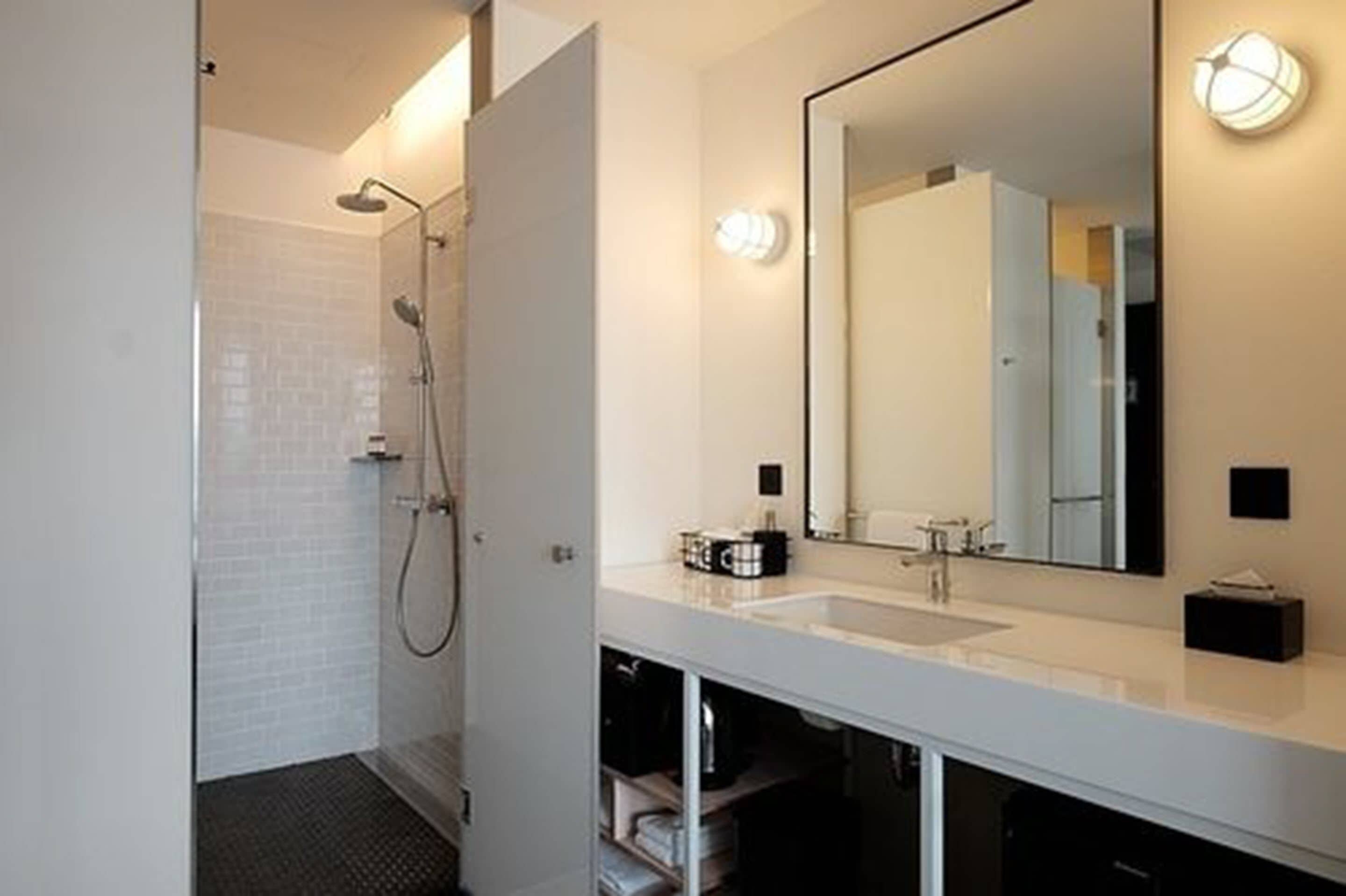 Ein modernes Badezimmer mit einer gläsernen Duschkabine, einem weißen Waschbecken und einem großen Spiegel.