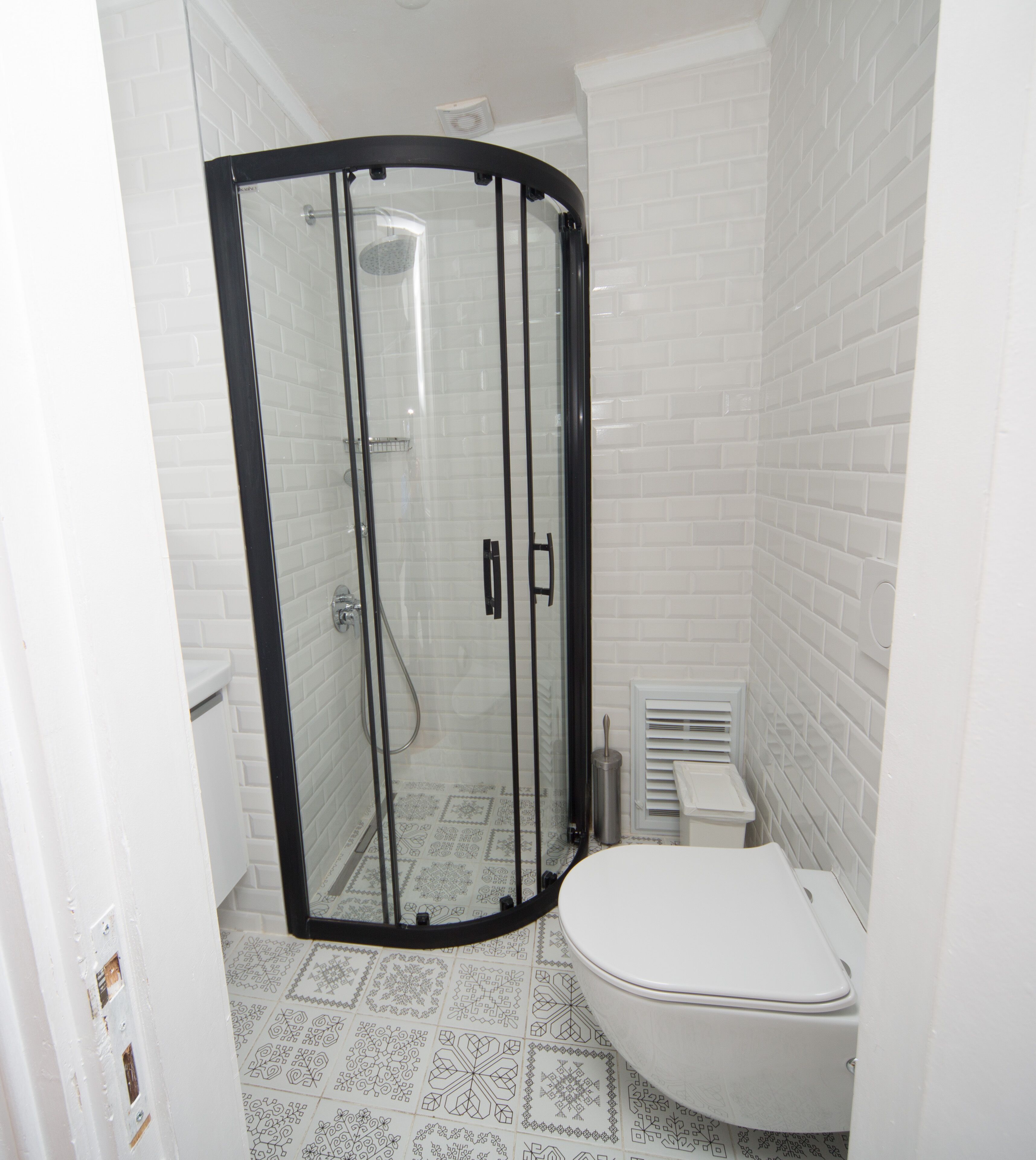 A bathroom with a glass-enclosed shower, a toilet, and patterned floor tiles.