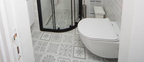 A bathroom with a glass-enclosed shower, a toilet, and patterned floor tiles.