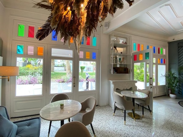 A room with a round table and chairs, a bookshelf, and a view of the garden through the windows. - Cenar Konak Butik Hotel (Adalar)
