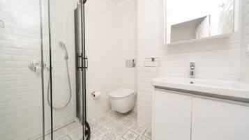 A modern bathroom with a glass shower enclosure, a white toilet, and a sink with a mirror above.