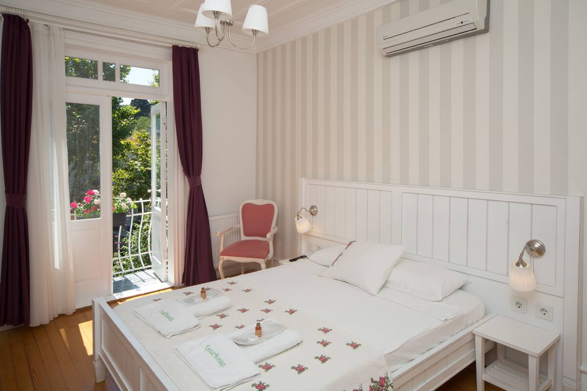 Un dormitorio con una cama grande, una silla, una mesita de noche y un ventanal con cortinas.