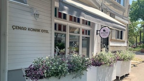A building with a sign reading "ÇENAR KONAK OTEL" and another sign for "leBONN coffee". There are flower planters in front of the building. - Cenar Konak Butik Hotel (Adalar)