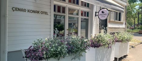 A building with a sign reading "ÇENAR KONAK OTEL" and another sign for "leBONN coffee". There are flower planters in front of the building.