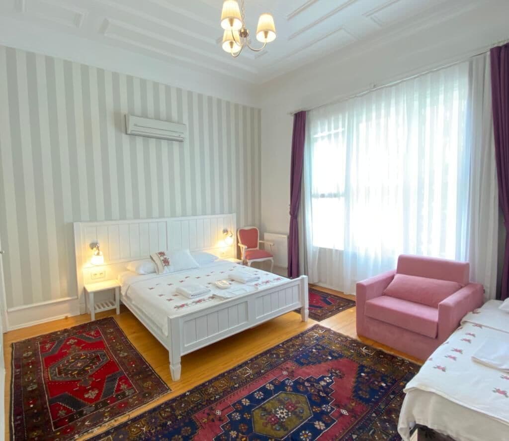 Un dormitorio con una cama blanca, una silla rosa y un ventanal con cortinas.