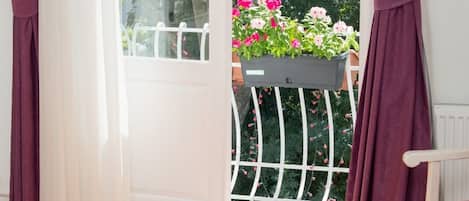 Una habitación con un amplio ventanal corredizo que da a un balcón con barandal blanco y una maceta colgante.