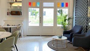 A spacious living room with a chandelier, a dining area with a white table and chairs, and a large window with colorful panes. - Cenar Konak Butik Hotel (Adalar)