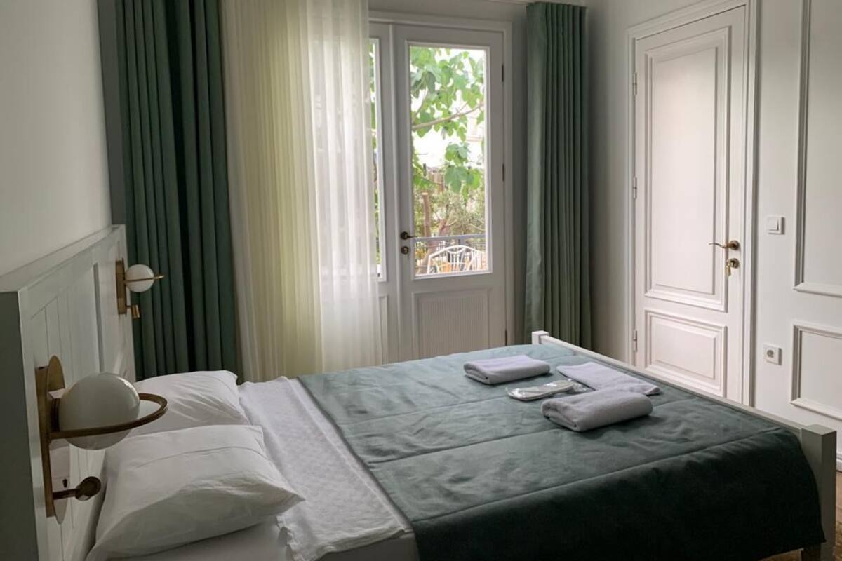 Una habitación de hotel con una cama, una ventana con cortinas, una puerta y una lámpara.