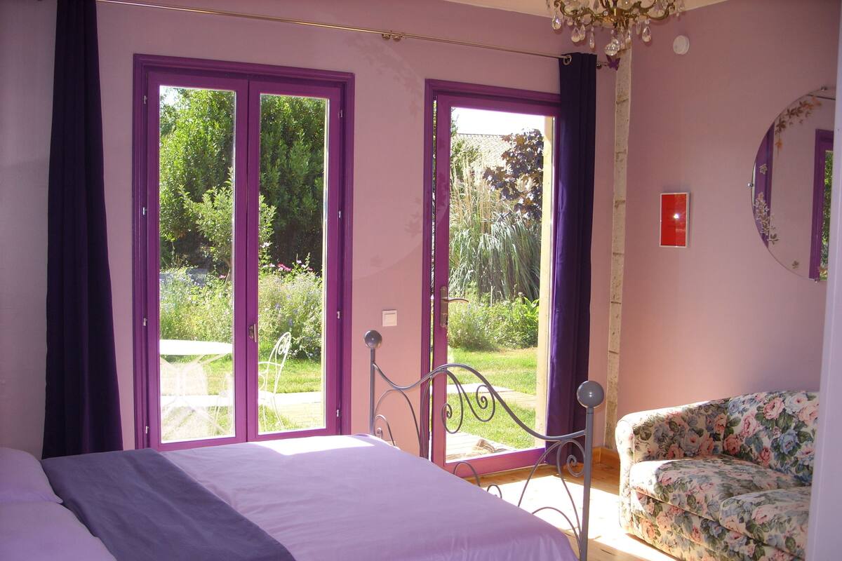 Un dormitorio con cama, una silla y vistas a un jardín a través de amplios ventanales.