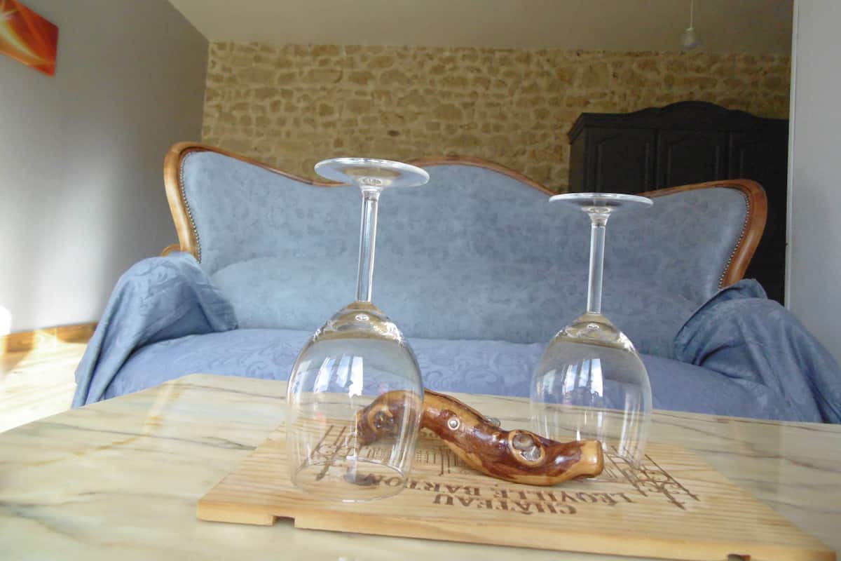 Una habitación con pared de piedra, un sofá azul y dos copas de vino sobre un posavasos de madera.