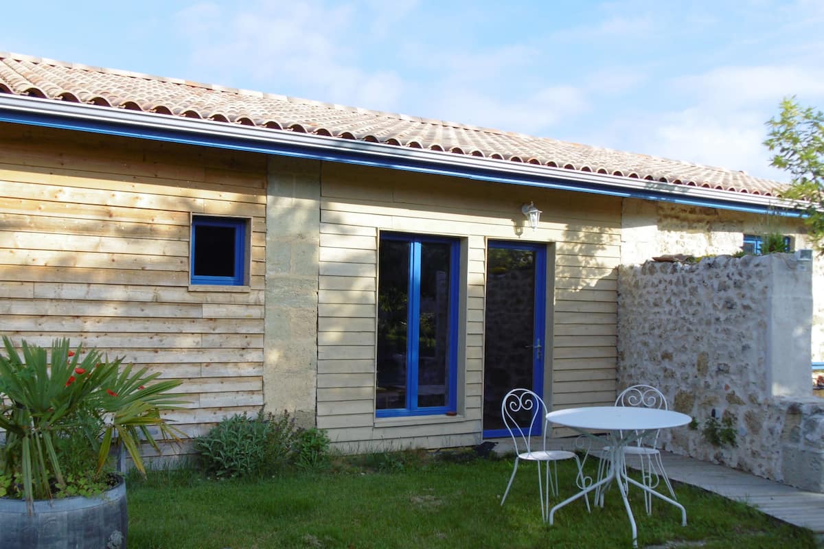Una casa con techo de tejas, pared de piedra y un pequeño patio con mesa y sillas.