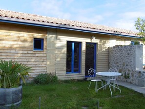 Una casa con techo de tejas, pared de piedra y un pequeño patio con mesa y sillas.