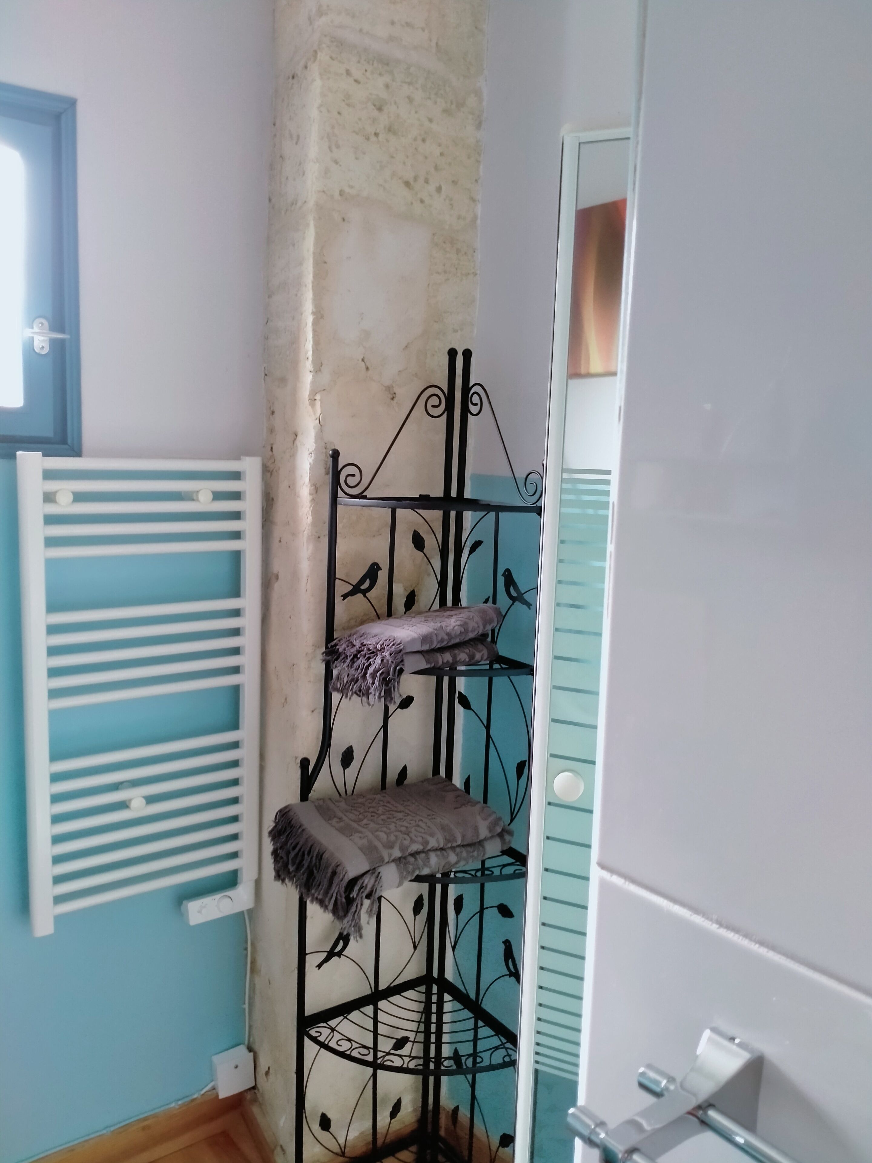A corner of a room with a white radiator, a blue door, and a black metal shelf with two cushions.