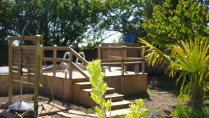 A wooden deck with steps leading up to a raised platform, surrounded by lush greenery and trees. - La Cadournaise (Saint-Seurin-de-Cadourne)
