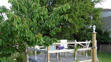 Une terrasse en bois avec une rambarde en métal, entourée d’une végétation luxuriante et d’arbres.