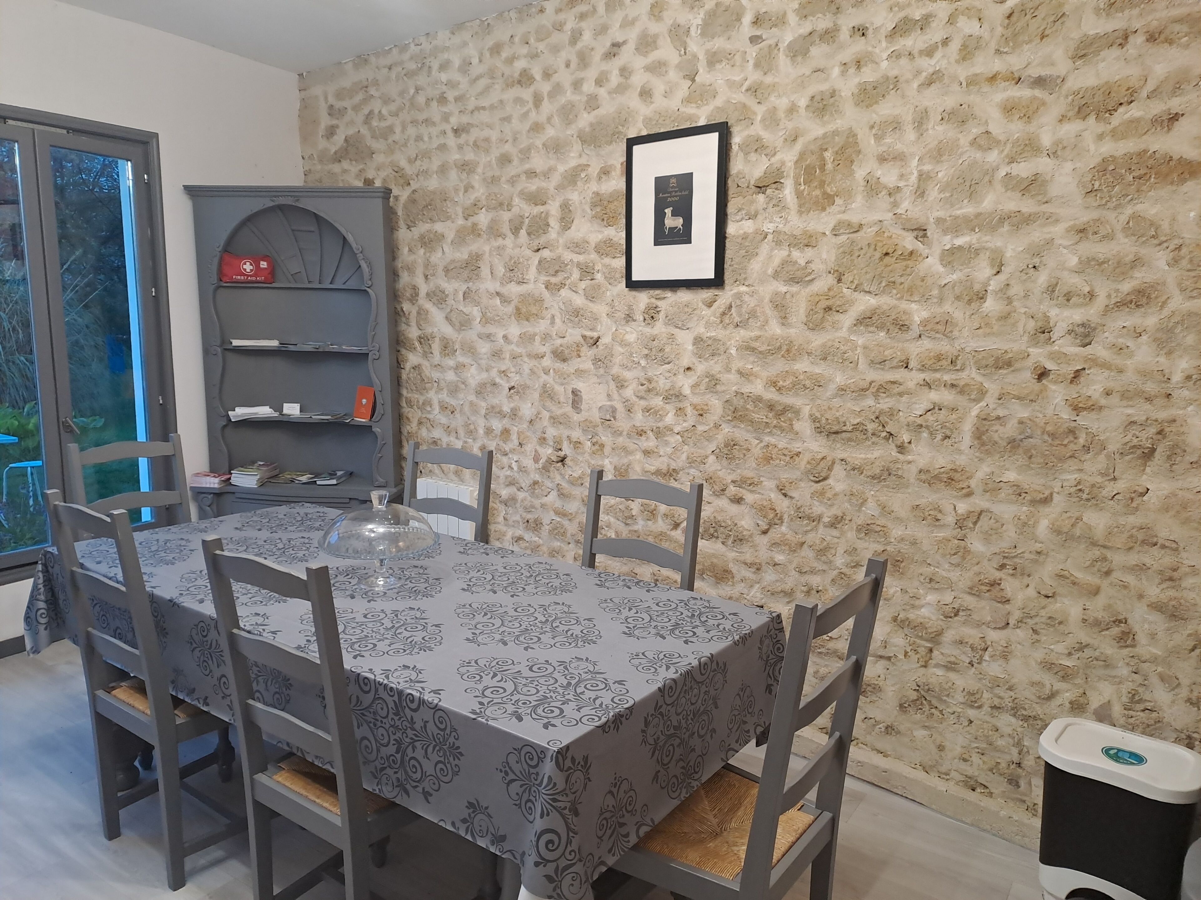 Un comedor con pared de piedra, un certificado enmarcado en la pared y un botiquín en un estante.