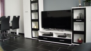 Una sala de estar moderna con televisor de pantalla plana, mueble de entretenimiento blanco y negro y sillones de cuero negro.