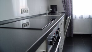 Una cocina moderna con encimera de acero inoxidable, horno empotrado y ventana con cortinas.