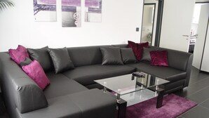 Una sala moderna con un sofá modular, una mesa de centro de vidrio y un tapete morado.