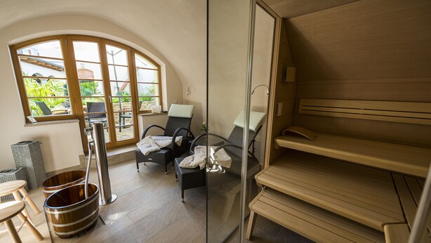 A spa room with a sauna, two chairs, a wooden bench, and a large window with a view of greenery. - Appart.Bog2 (Görlitz)