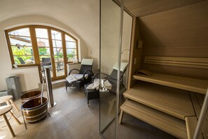 Kylpyhuoneessa on sauna, kaksi tuolia, puinen penkki ja suuri ikkuna, josta avautuu näkymä vehreään maisemaan.