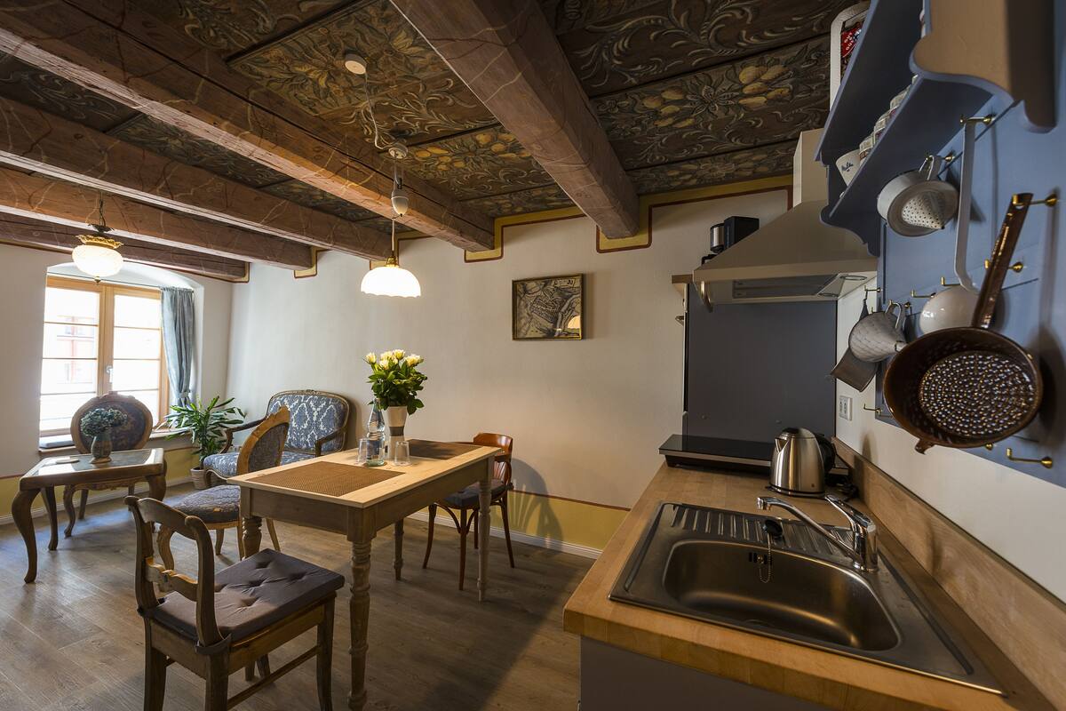 A kitchen with wooden beams, a sink, and a dining area with chairs and a table.