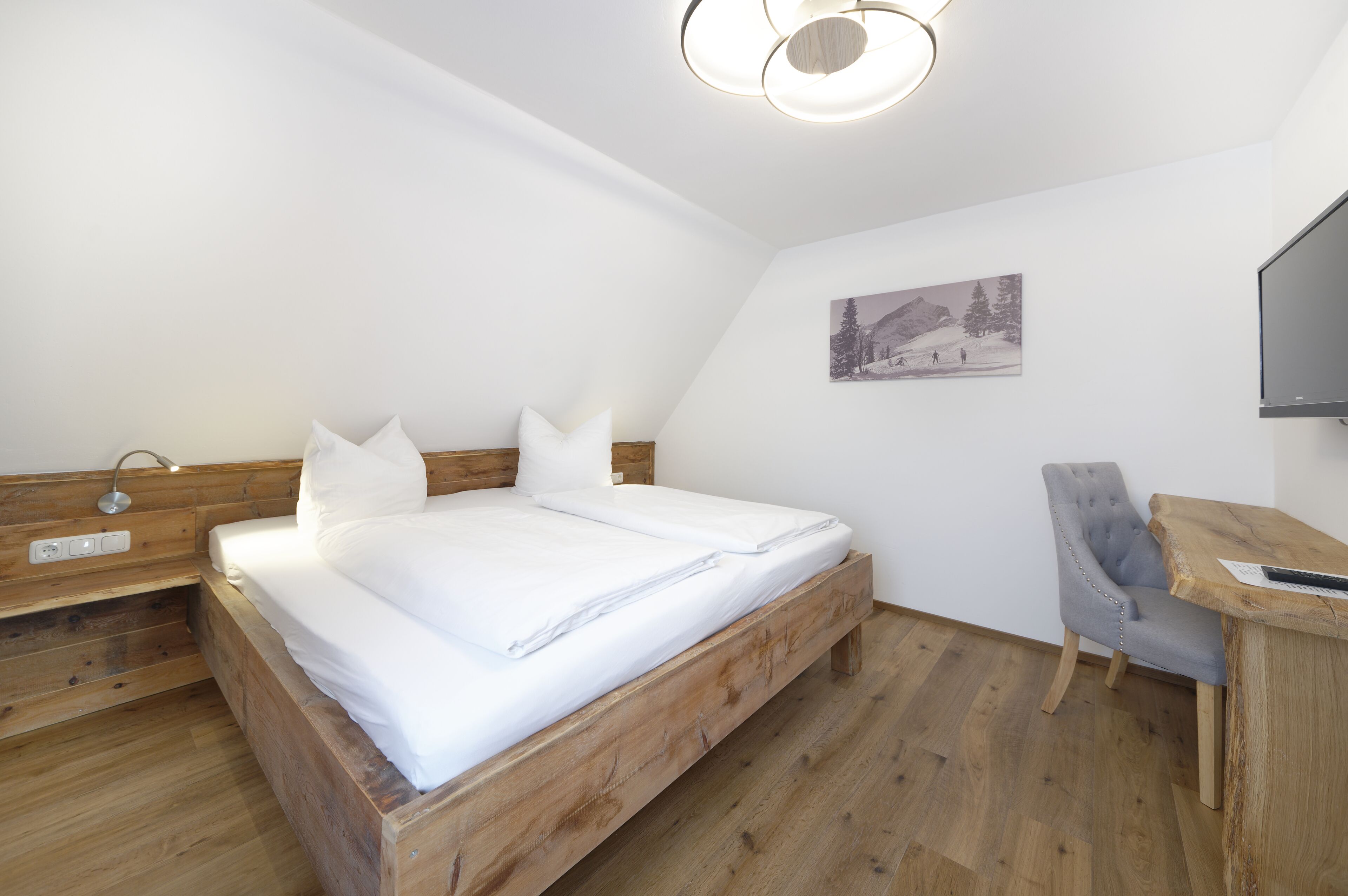 Quarto com cama de madeira, uma escrivaninha e uma cadeira.