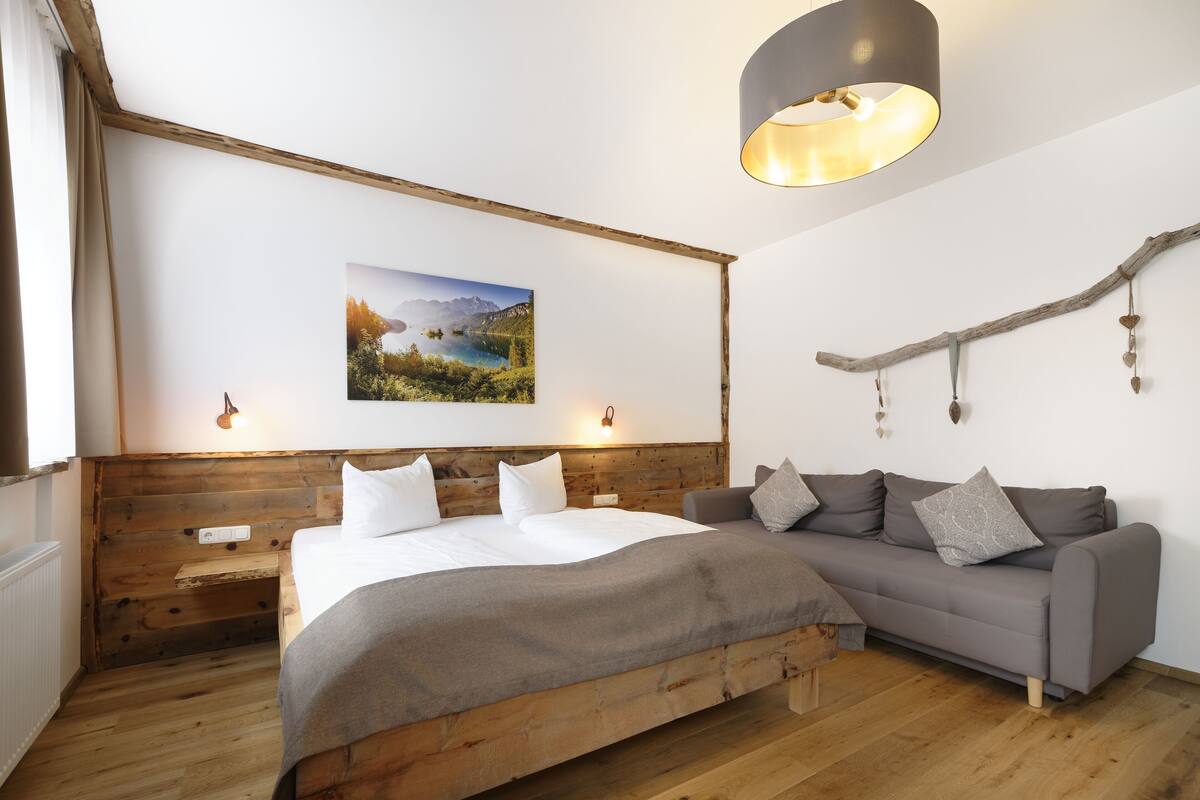 A bedroom with a wooden bed, a gray sofa, a wall-mounted picture, and a hanging branch decoration.