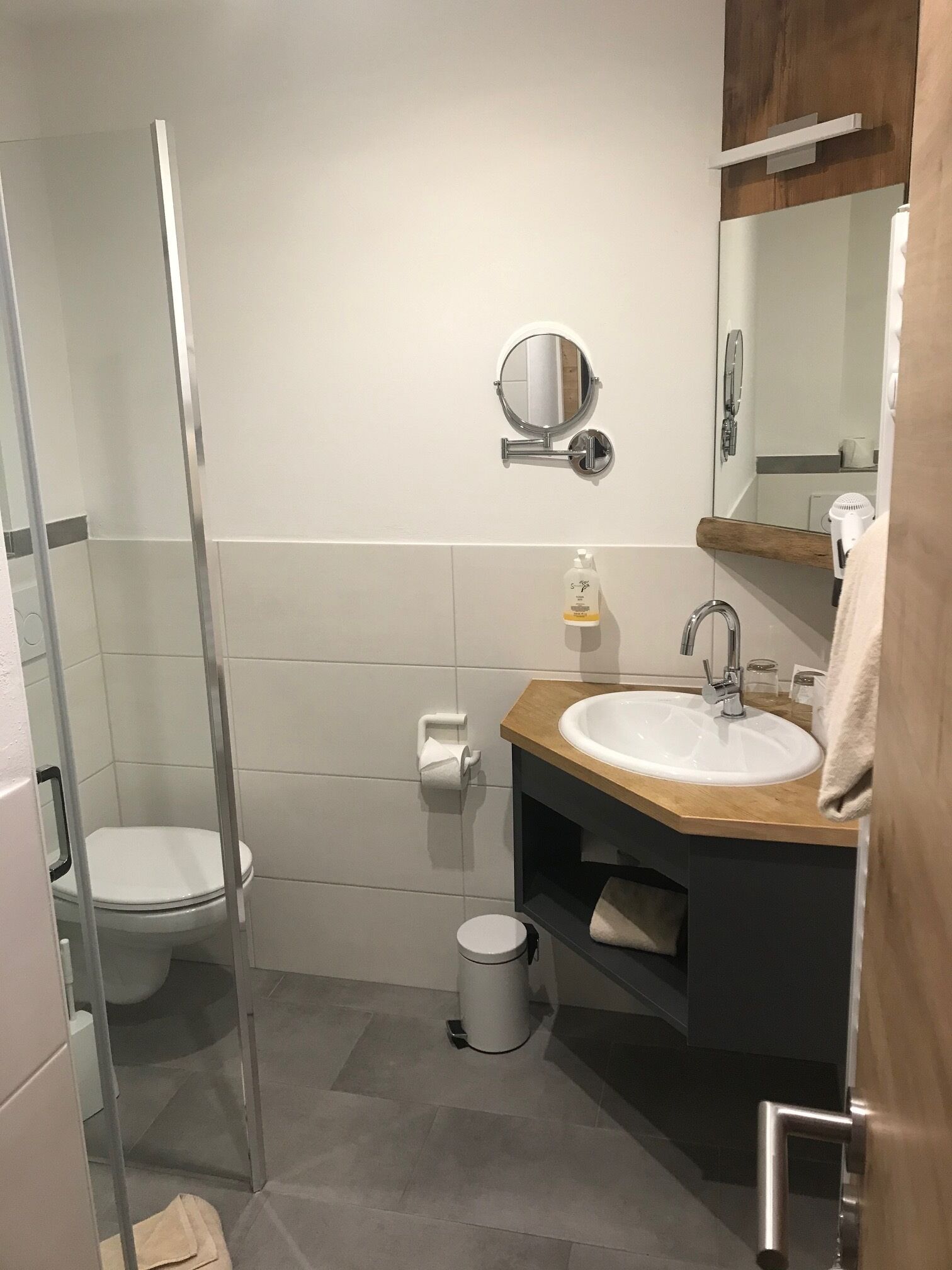 A modern bathroom with a glass shower enclosure, a white toilet, a sink with a wooden countertop, and a mirror above the sink.