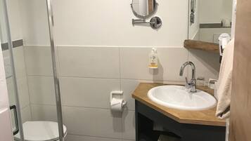 A modern bathroom with a glass shower enclosure, a white toilet, a sink with a wooden countertop, and a mirror above the sink.
