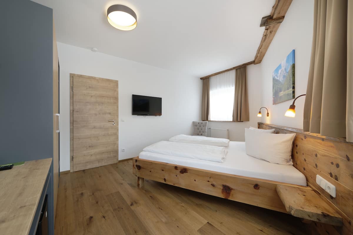 A bedroom with a wooden bed, a television, a window with curtains, and a painting on the wall.