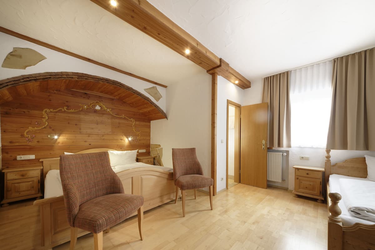 A bedroom with a wooden headboard, two chairs, a bed, a nightstand, and a window with curtains.